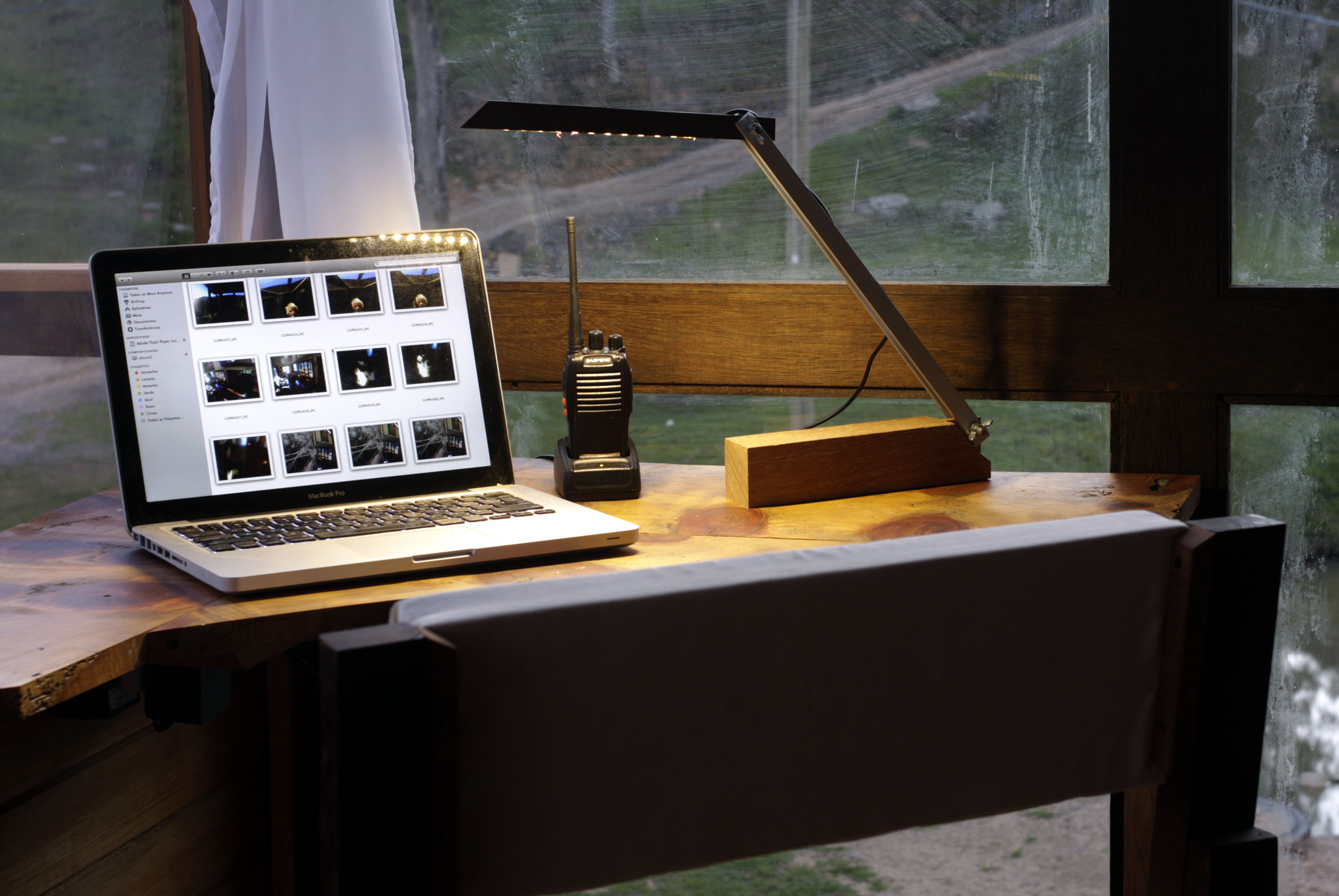 Lap top aberto sobre mesa da escrivaninha da casinha, com luminária e rádio de comunicação