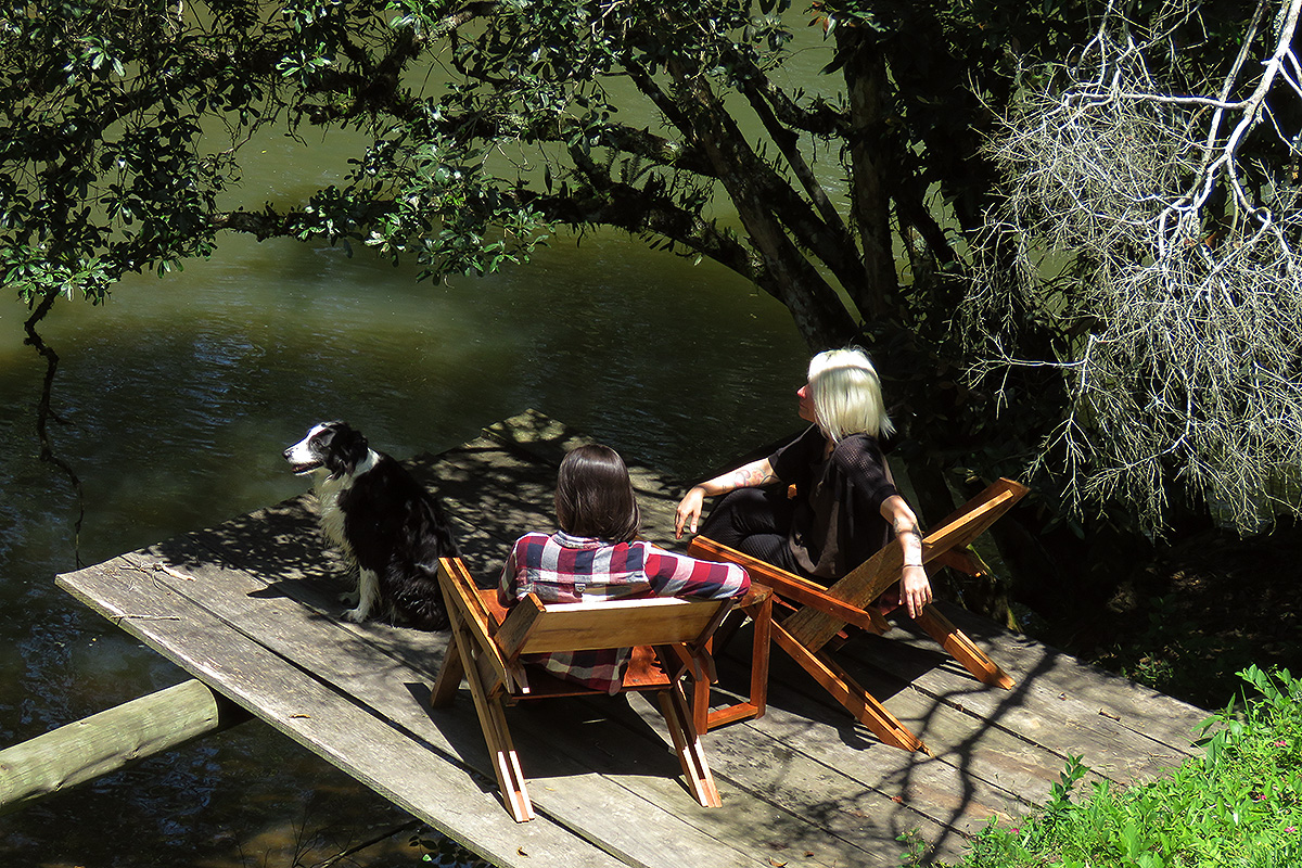 Duas jovens e uma cachorra sobre o deque de madeira sobre o Rio, perto da casa da cama