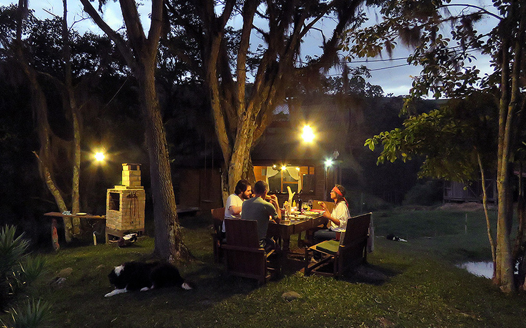 Família durante refeição ao anoitecer na Cozinha ao ar livre junto da Casinha, uma das unidades da Pousada Pedras Rollantes, em Alfredo Wagner
